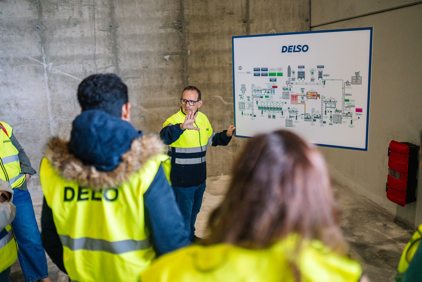 Grupo de asistentes con chalecos de DELSO escuchando la explicación del esquema de la planta en la fábrica de Burgos